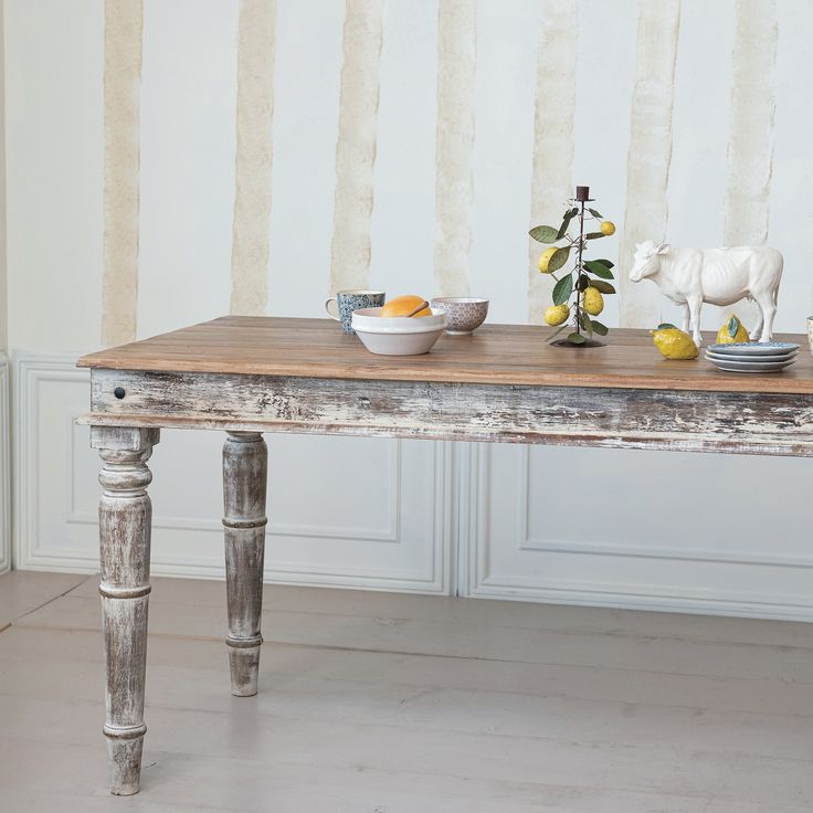 an old table with bowls and fruit on it in front of a striped wallpaper