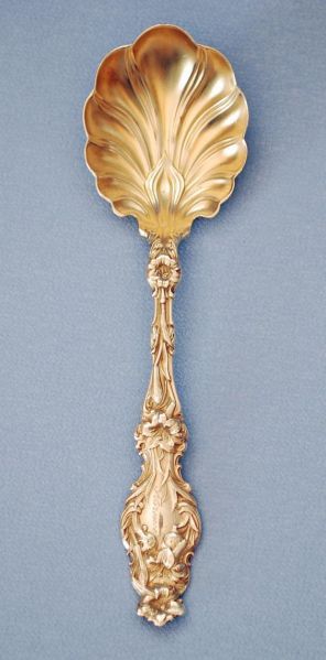 an ornate gold plated spoon on a blue background, with the handle in the shape of a flower