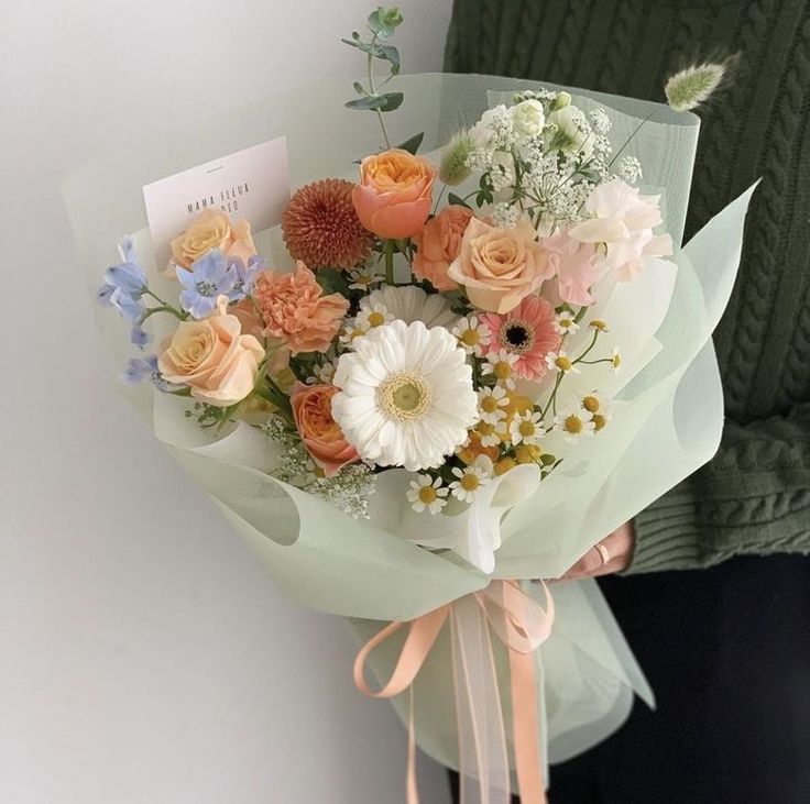 a person holding a bouquet of flowers in their hands with a card attached to it