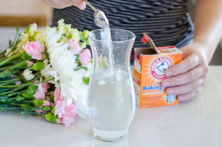 a person pouring water into a glass next to flowers and a box of baking soda