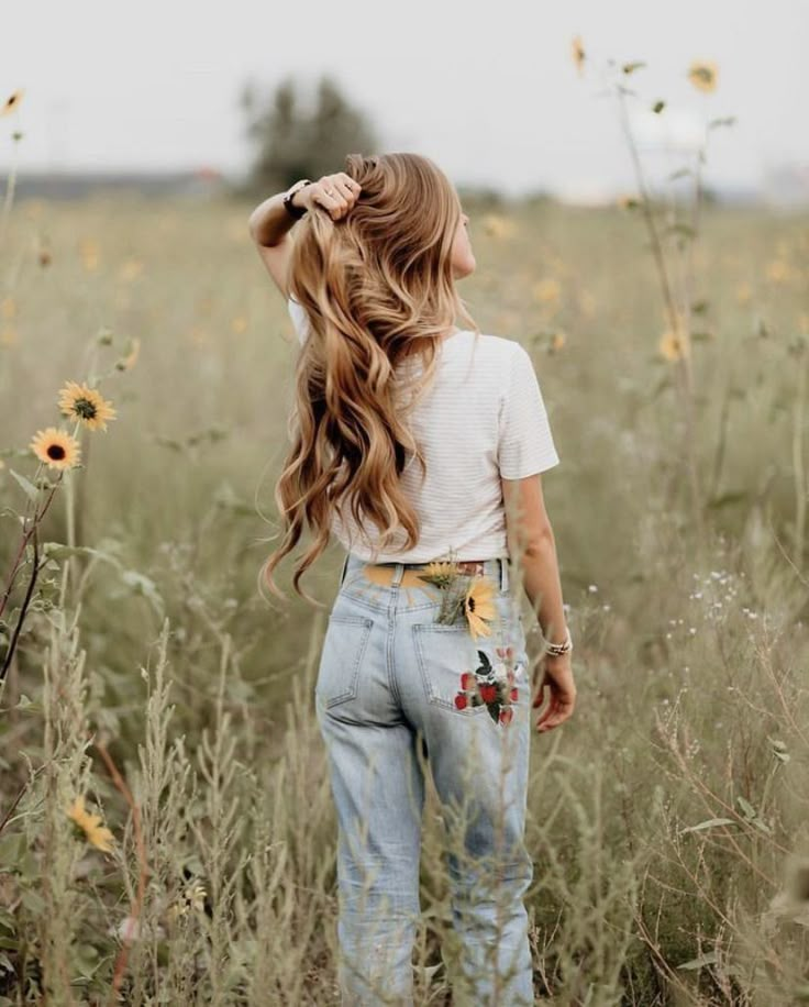 a woman with long hair standing in the middle of a field full of sunflowers