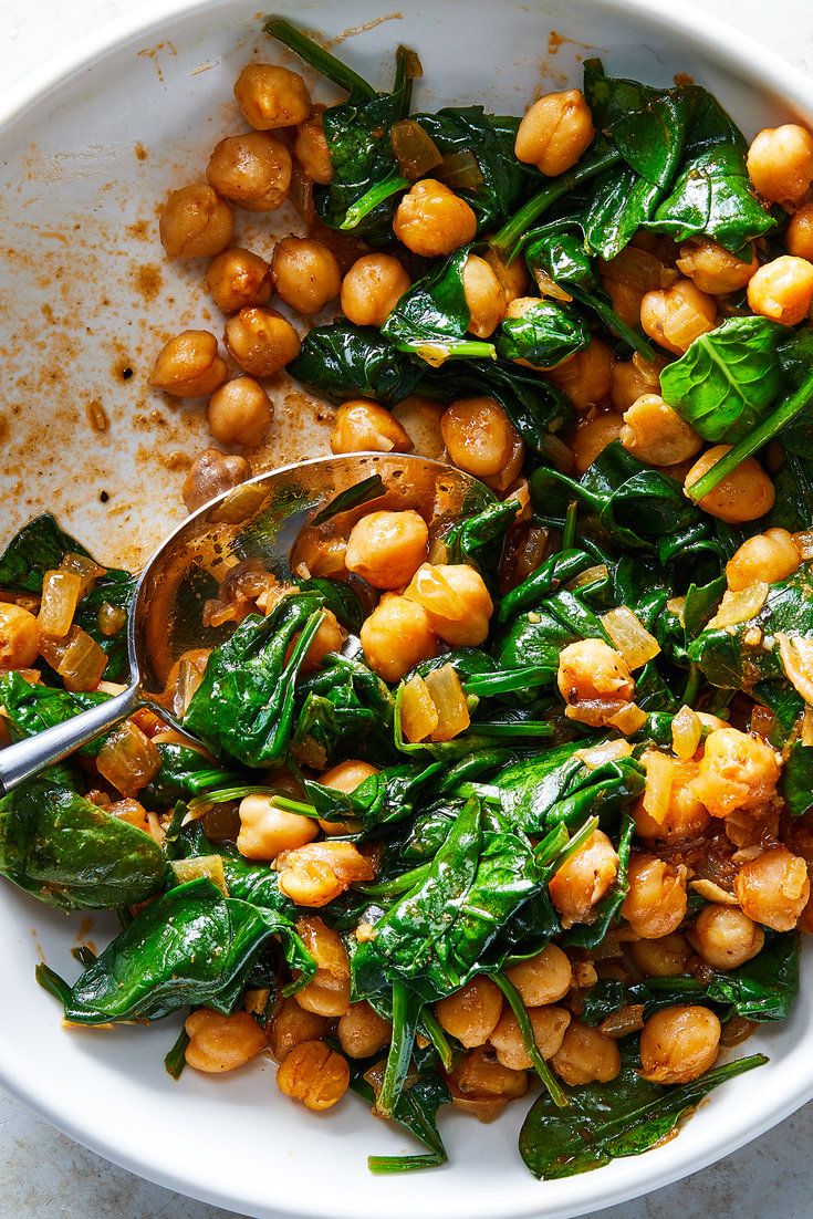 a white bowl filled with spinach and chickpeas on top of a table