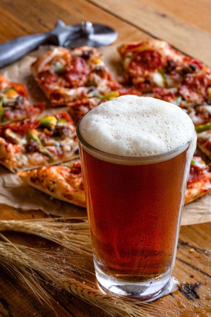 a glass of beer sitting on top of a wooden table next to slices of pizza