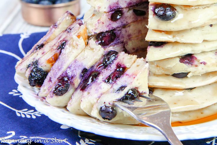 a stack of blueberry pancakes on a plate with a knife and fork next to it