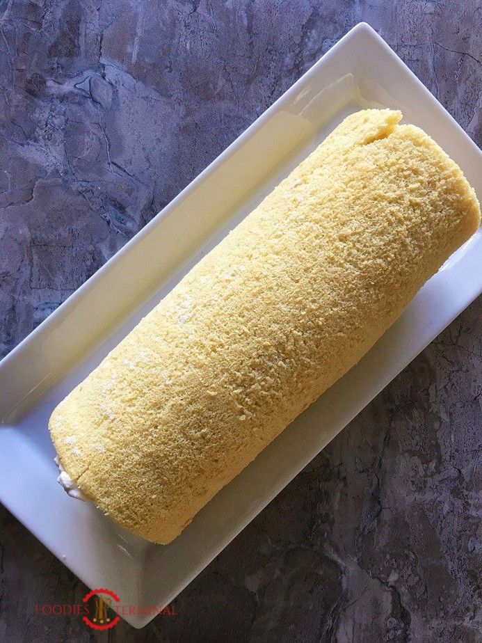 a long piece of food on a white plate next to a gray stone wall and floor