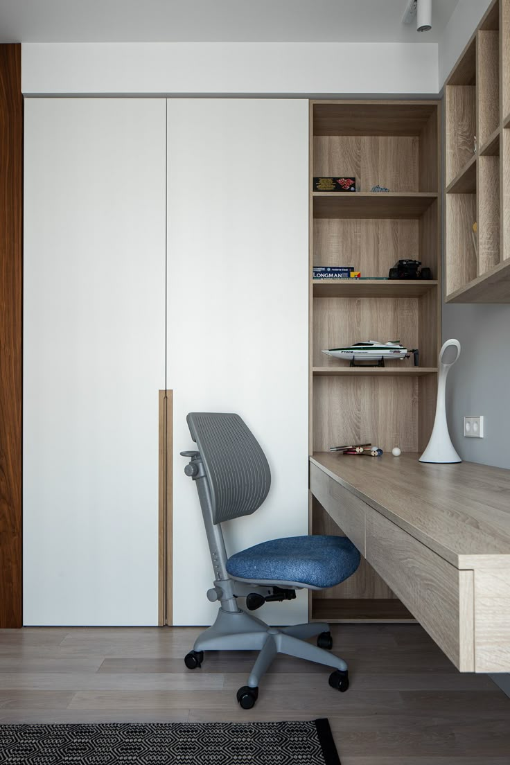 a blue office chair sitting in front of a wooden desk and bookshelf next to a white wall