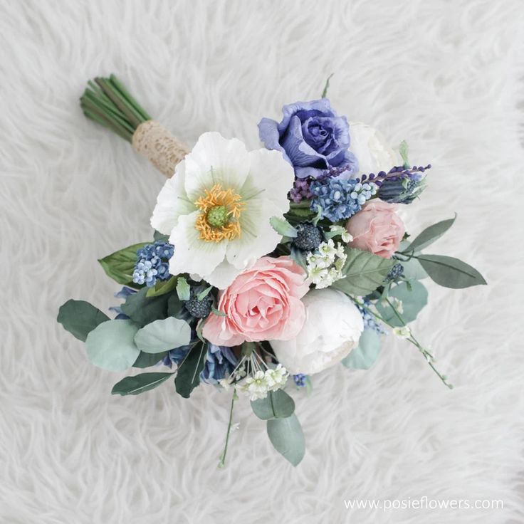 the bridal bouquet is laid out on a white furnishing area with blue and pink flowers