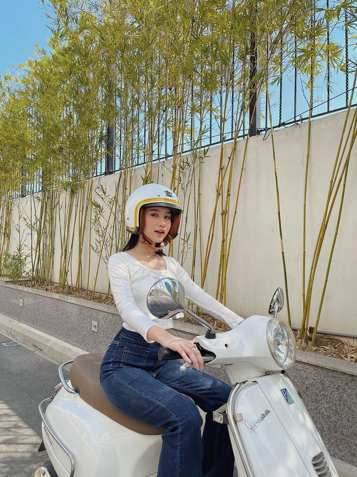 a woman sitting on top of a white scooter next to a bamboo tree