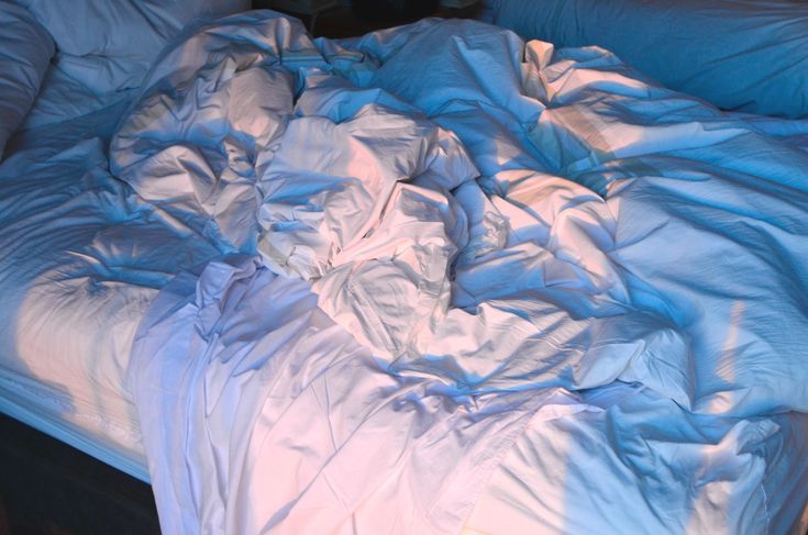 an unmade bed with white sheets and blue comforter on the bottom half is shown