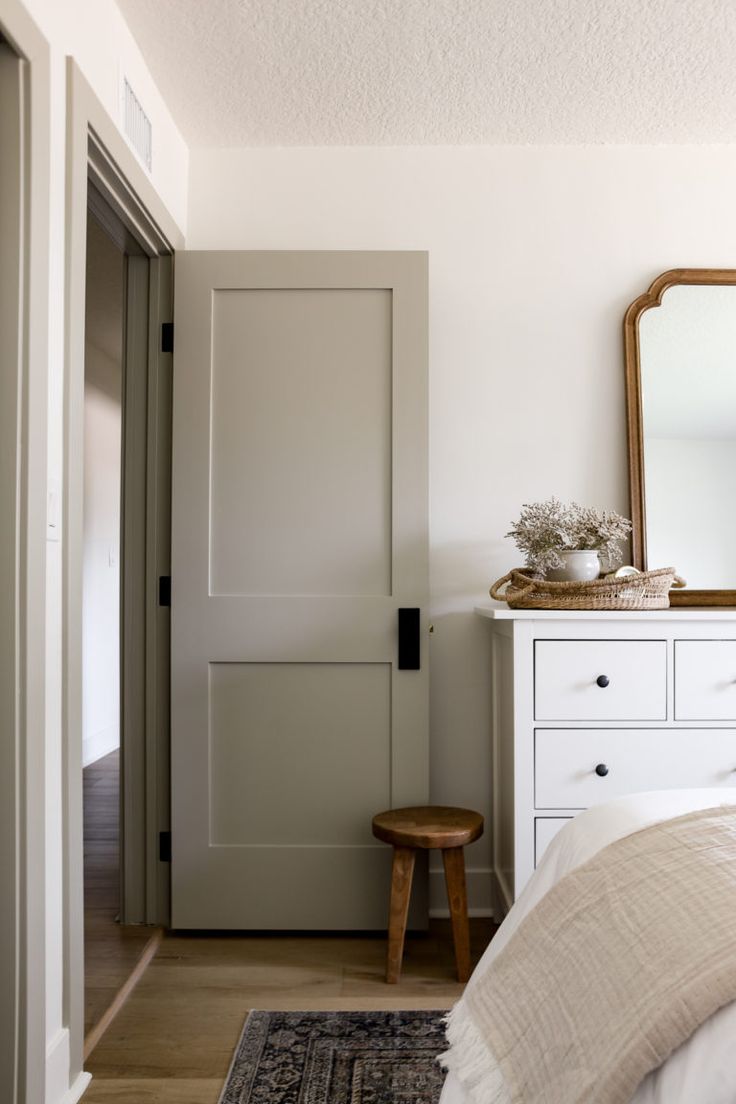 a bedroom with a bed, dresser and mirror in it's corner next to an open door