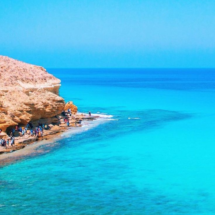 people are standing on the edge of a cliff by the ocean with clear blue water