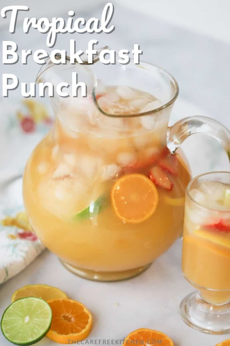 tropical breakfast punch in a pitcher with orange slices and limes next to it on a table