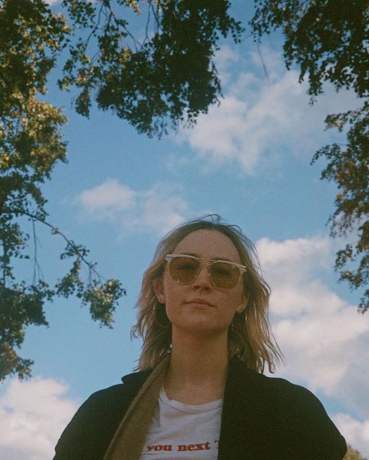 a woman wearing sunglasses standing in front of some trees