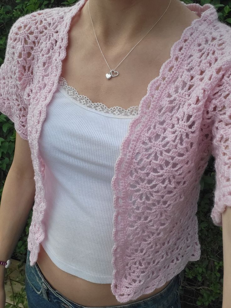 a woman is wearing a pink crochet shrugr jacket and white tank top