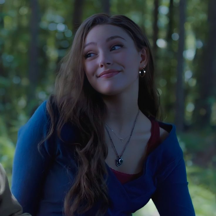 a young woman is sitting in the woods and smiling for the camera while wearing a blue shirt