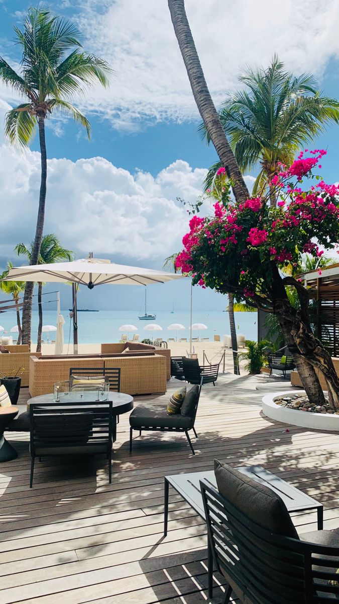 an outdoor seating area with chairs and umbrellas on the deck next to the ocean