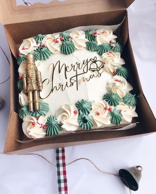 a christmas cake in a box with the words merry christmas written on it, surrounded by holiday decorations