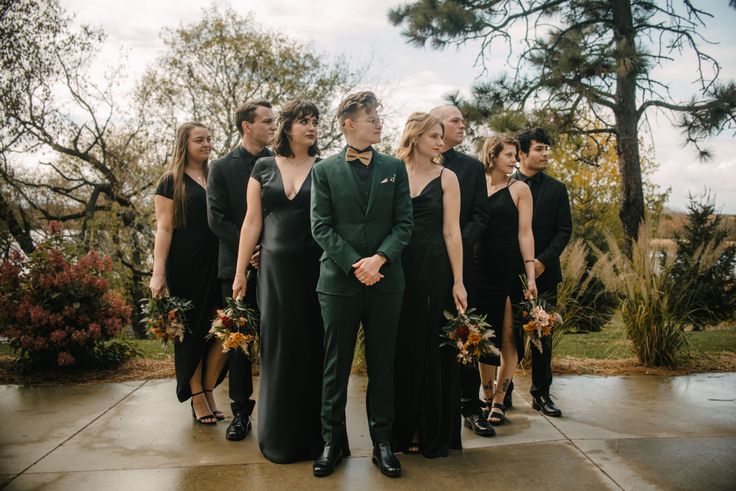 a group of people standing next to each other in front of trees and bushes with one person wearing a green suit