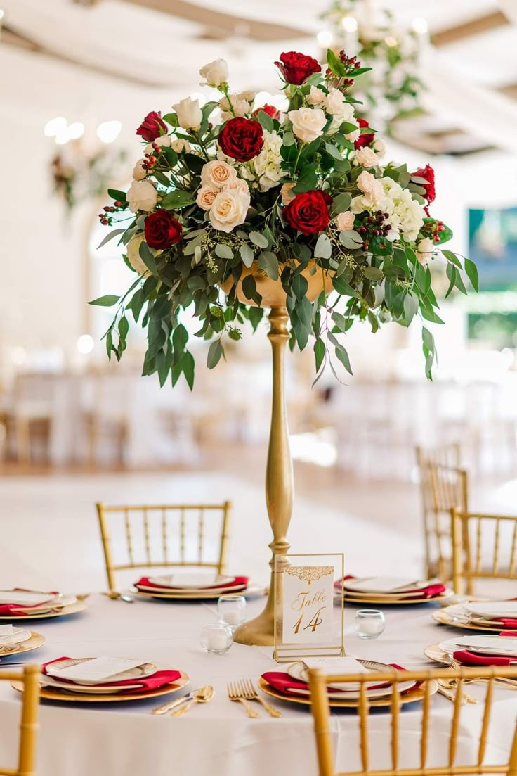 an elegant centerpiece with red and white flowers on a gold pedestal at a wedding reception