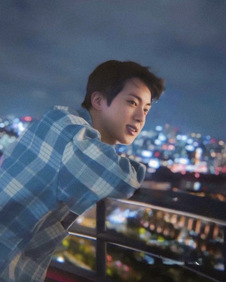 a young man standing on top of a roof next to a cityscape at night