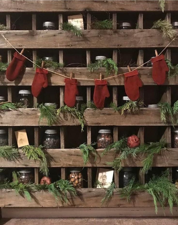 christmas stockings hanging on a wooden pallet filled with jars and spices, surrounded by greenery