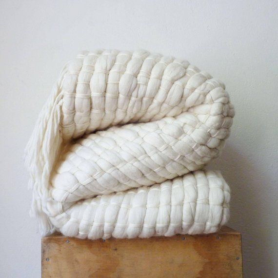 two white blankets stacked on top of each other next to a wooden box and wall