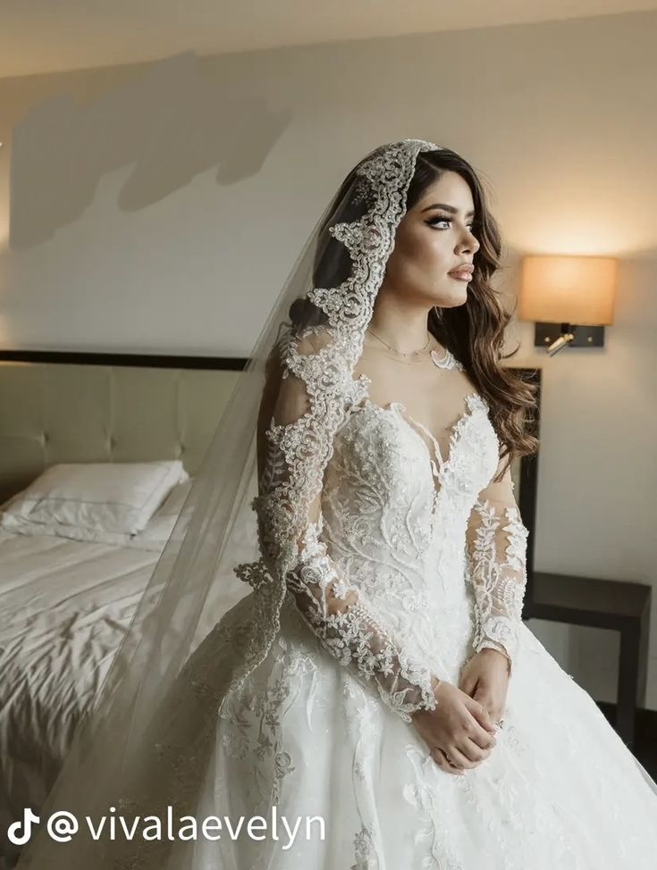 a woman in a wedding dress is standing near a bed with her veil pulled back