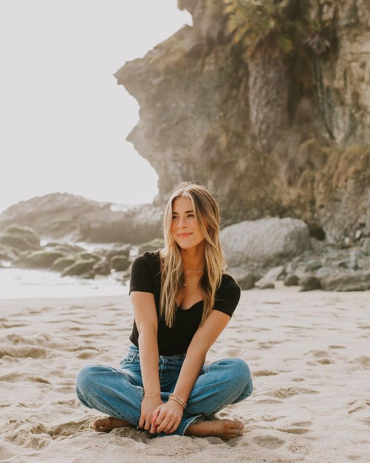 a woman is sitting on the beach with her legs crossed and looking at the camera