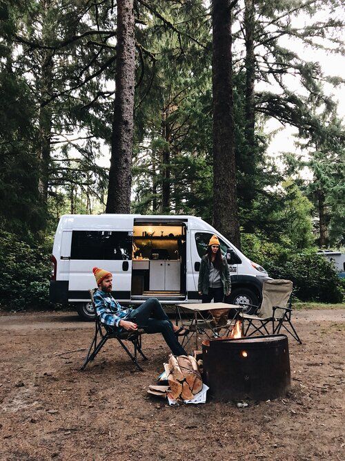 a man sitting in a chair next to a campfire with a van behind him