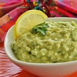 a white bowl filled with guacamole on top of a table next to a slice of lemon