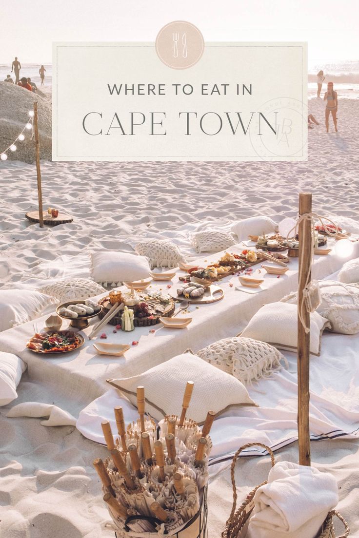 a table set up on the beach for an event with white linens and pillows