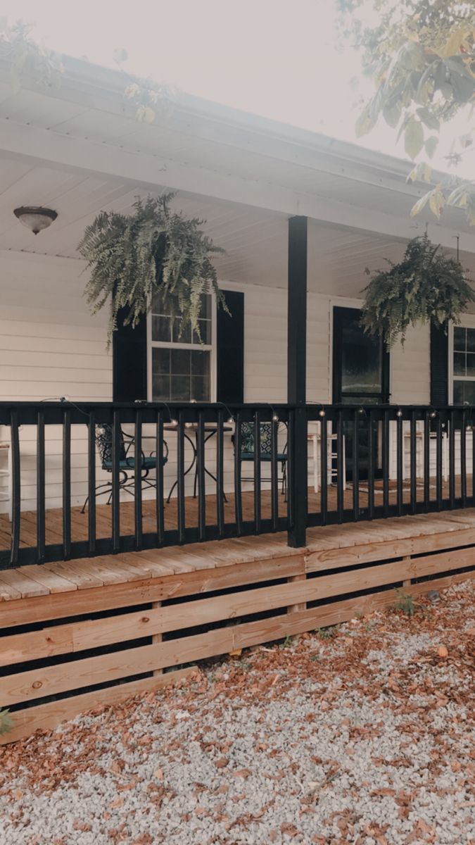 the front porch of a white house with black iron railings and potted plants