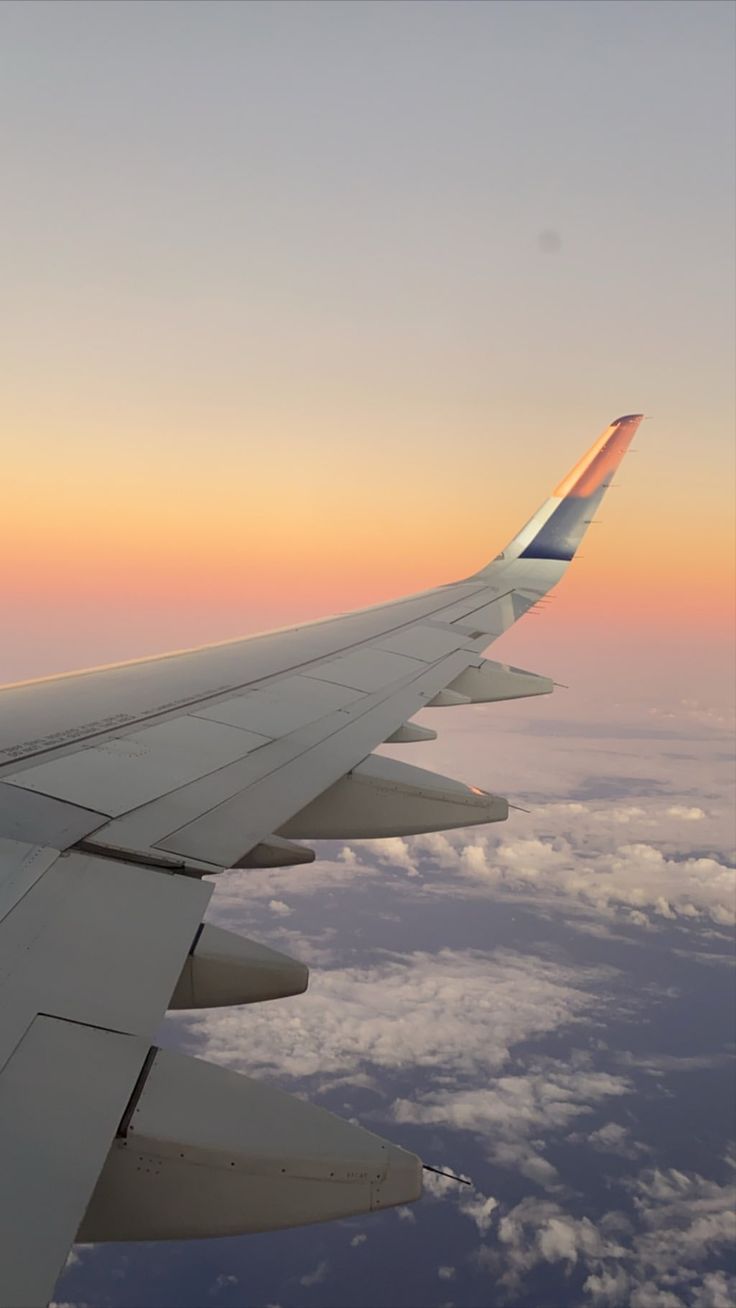 the wing of an airplane as it flies through the sky at sunset or dawn over clouds