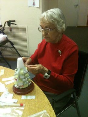 an older woman sitting at a table making a christmas tree out of paper machs