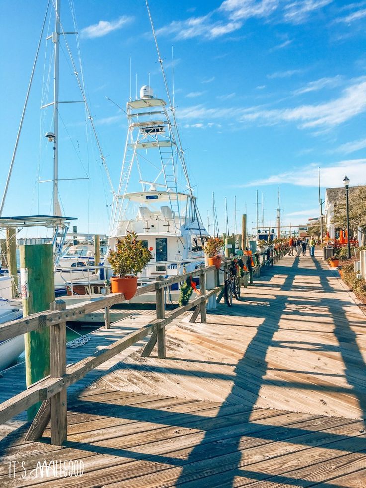 people are walking on the boardwalk near boats docked in the water and blue skies above them