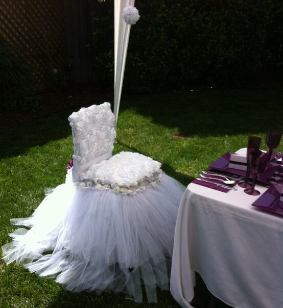 a white chair sitting on top of a lush green field next to a table covered in purple and white flowers