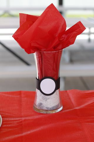 a glass vase with red tissue paper in it sitting on a table next to a cup