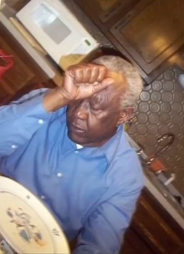 an older man sitting at a table with his hands on his head and looking up