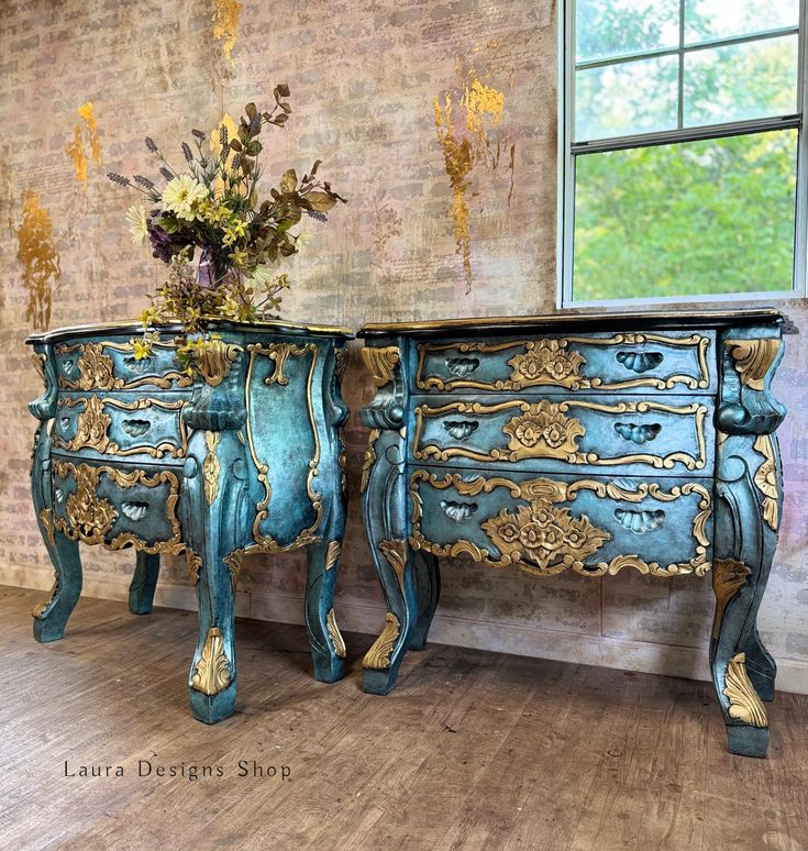 an ornate blue and gold painted dresser next to a window with flowers on it in front of a brick wall