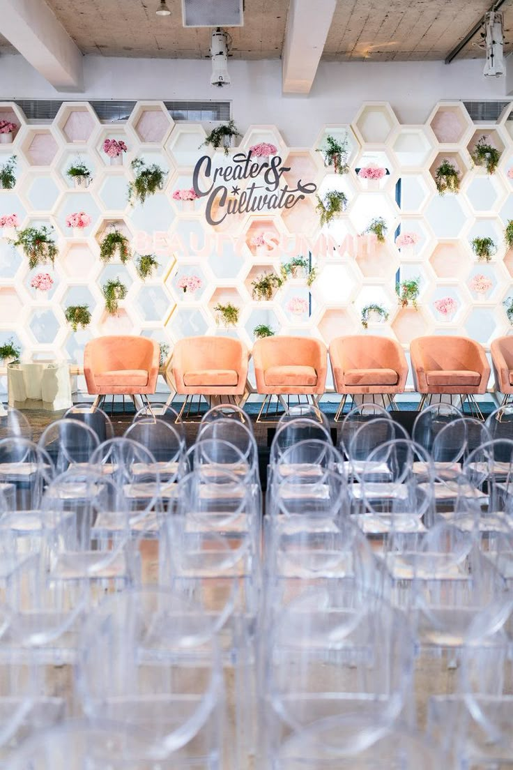 rows of clear plastic chairs in front of a wall with flowers and plants on it