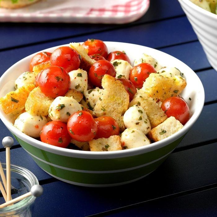 a bowl filled with tomatoes and bread on top of a blue table next to a glass container