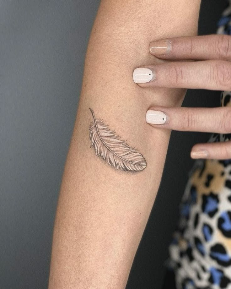 a woman's arm with a feather tattoo on the left side of her arm