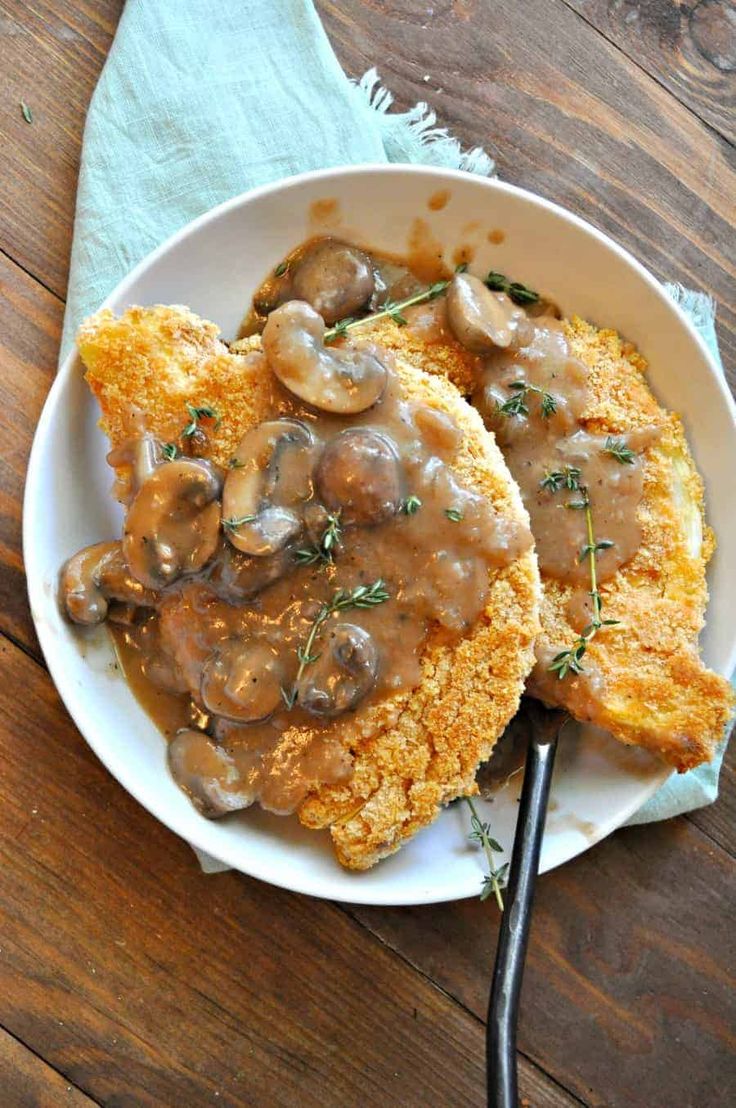 two pieces of chicken covered in mushroom gravy on top of a white plate