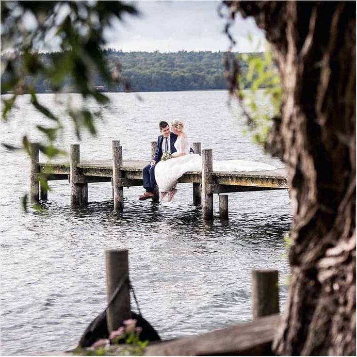 a bride and groom sitting on a dock in the water