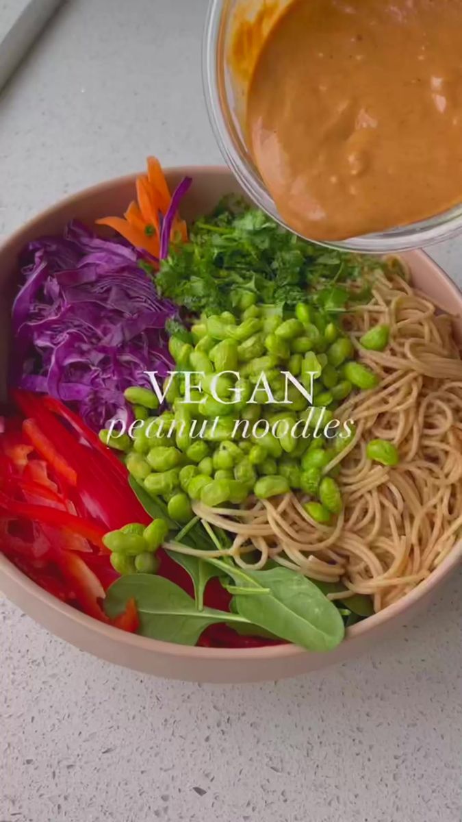 a bowl filled with noodles and vegetables next to a sauce in a glass container on top of a table