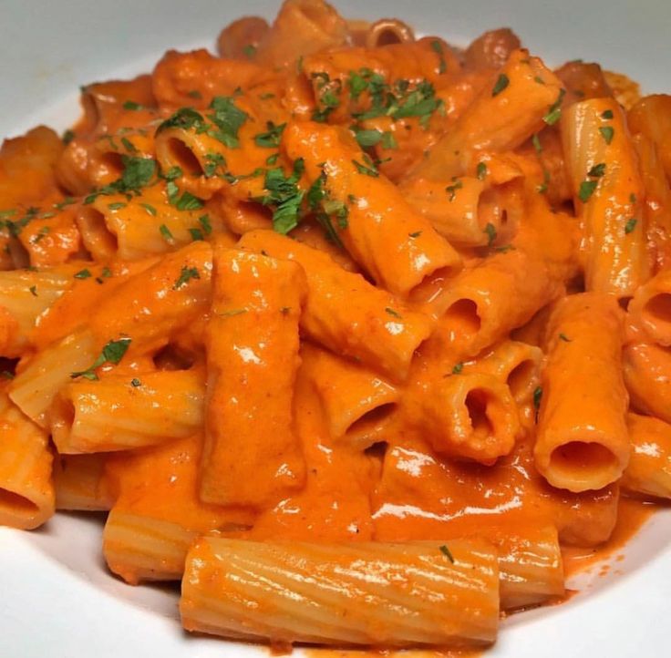 a white plate topped with pasta covered in sauce and garnished with parsley