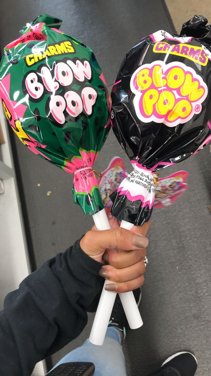 a person holding two lollipops in their hands and some candy on the other hand