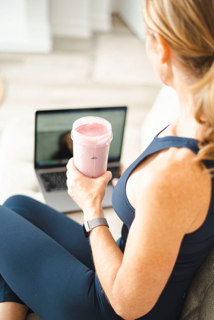 a woman sitting on a couch holding a pink cup in front of her laptop computer