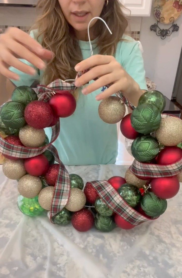 a woman is making a christmas wreath out of ornaments