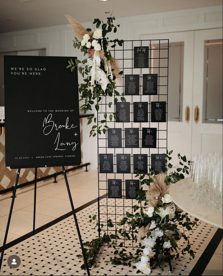 a sign with flowers and greenery on it next to a black and white checkered wall